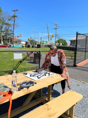 Jay Loo standing in front of a picnic table in the sun, creating in black marker on white poster